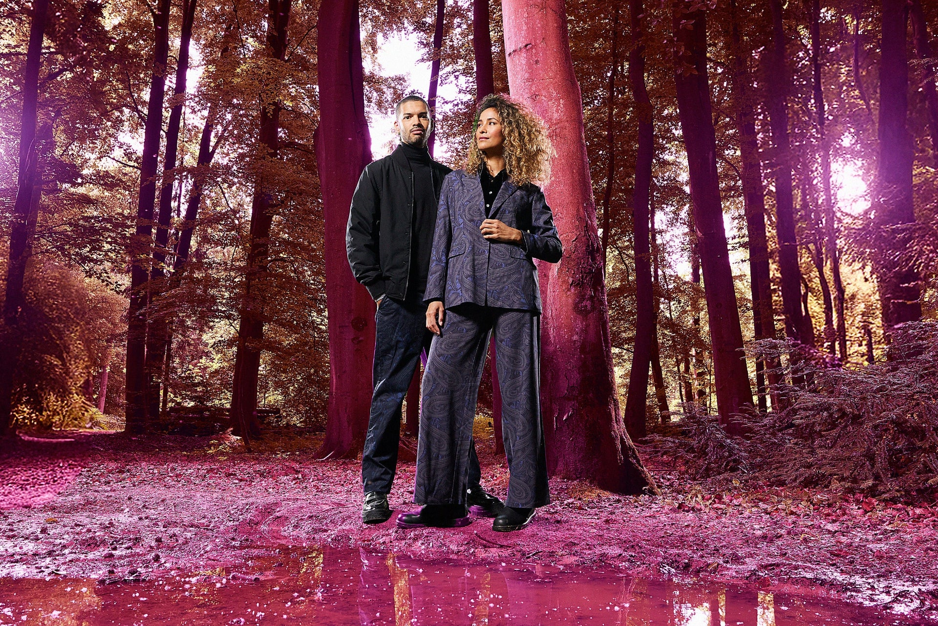 A nicely dressed couple standing in a forest with a surreal pink hue