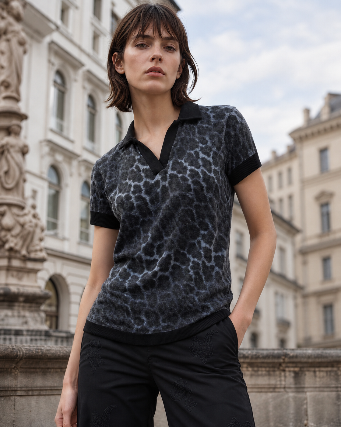 A woman in the Lords of Harlech Jessica sweater polo in leopard smoke in front of a Baroque facade